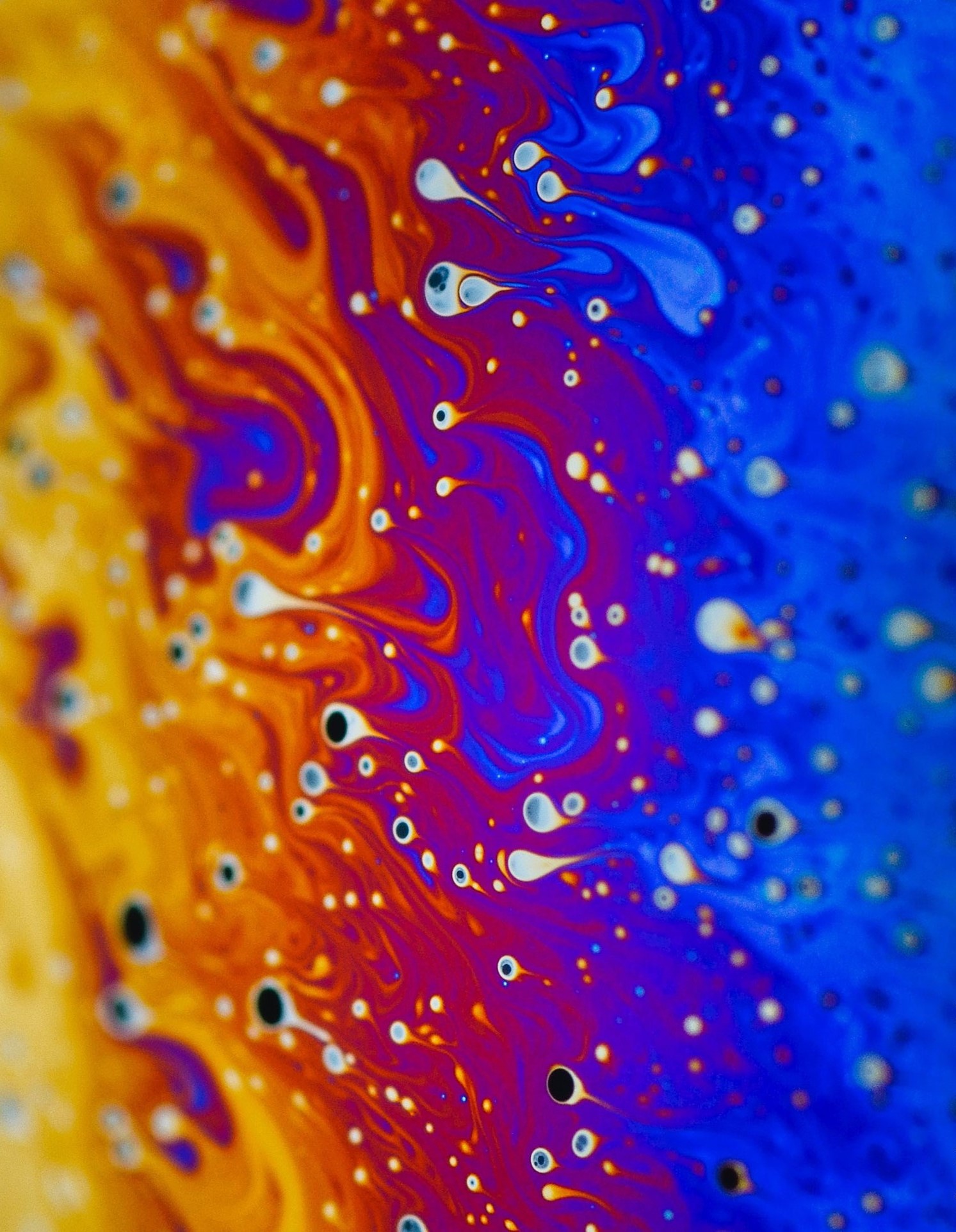 The image shows a mixture of water and soap. By illuminating the bubbles, electric shapes and colours are created. The waves of blue, orange and pink stand out.